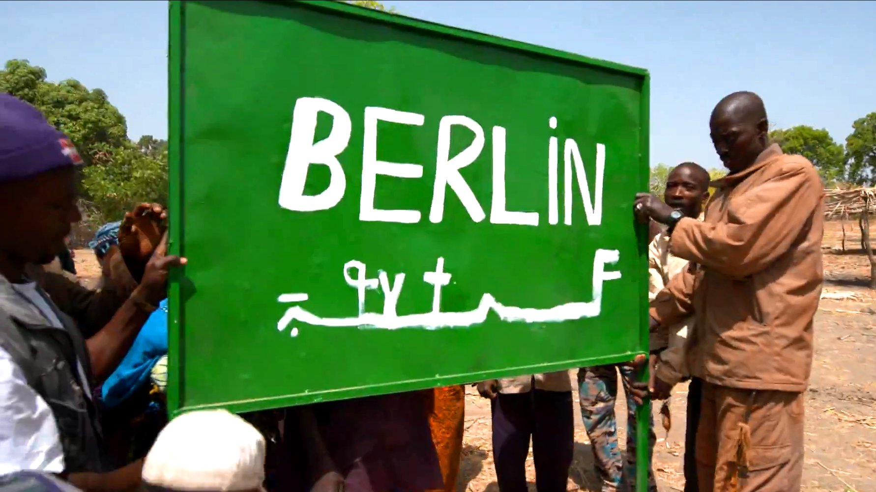 Bewohner von Berlin in Guinea halten ein Ortsschild hoch.